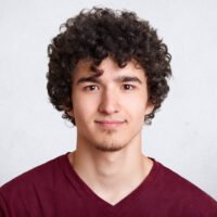 Close up portrait of curly handsome European male, wearing casual maroon shirt, isolated over white background, looking directly at camera, beig photographed in photo studio. People concept.